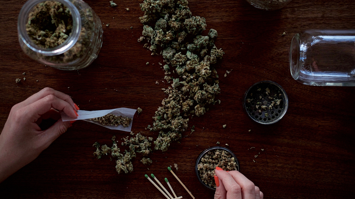 Personne roulant un joint de papier de marijuana sur une table en bois avec du cannabis qui traîne